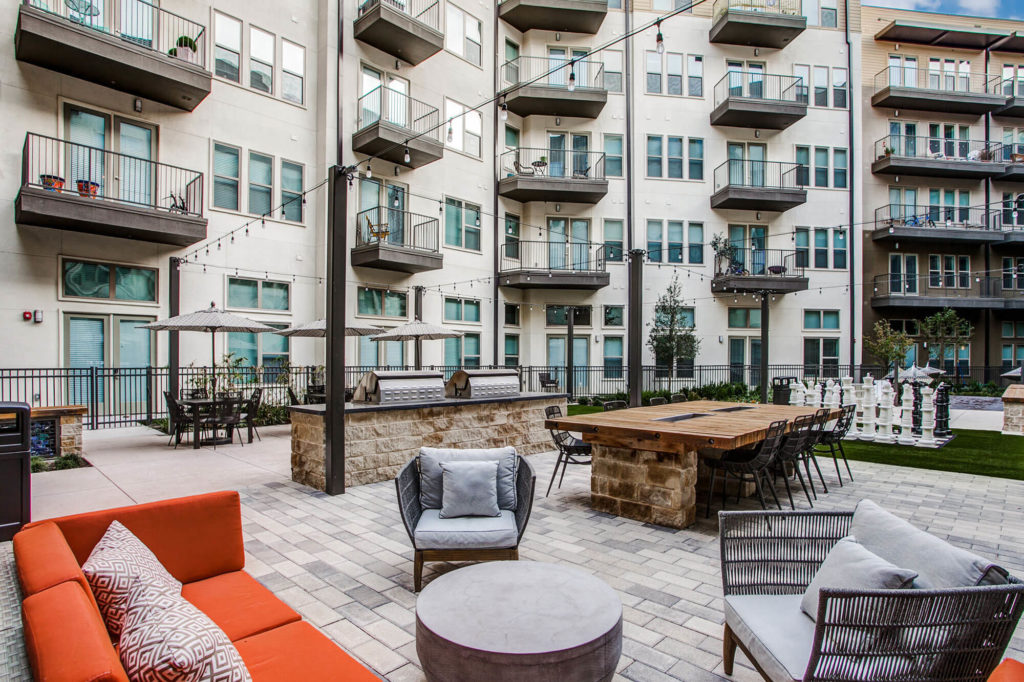 Outdoor community area with grills, plush seating, table seating, patio lights, and life-size chess game