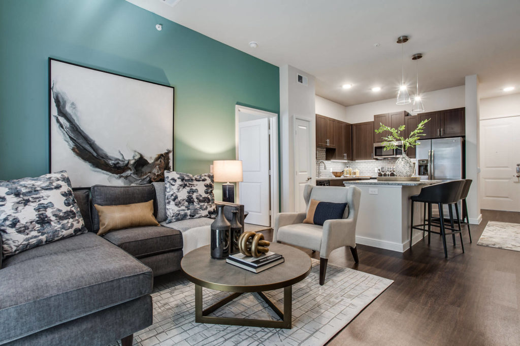 Open concept living room with wood-style floors, teal accent wall, open to kitchen with island, granite counters, and stainless-steel appliances