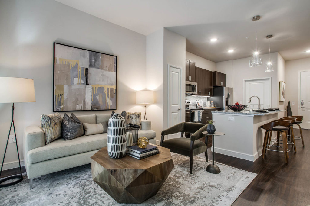 Living room with wood-style floors and modern furniture, open to kitchen with large island, granite counters, pendant lighting, and stainless-steel appliances