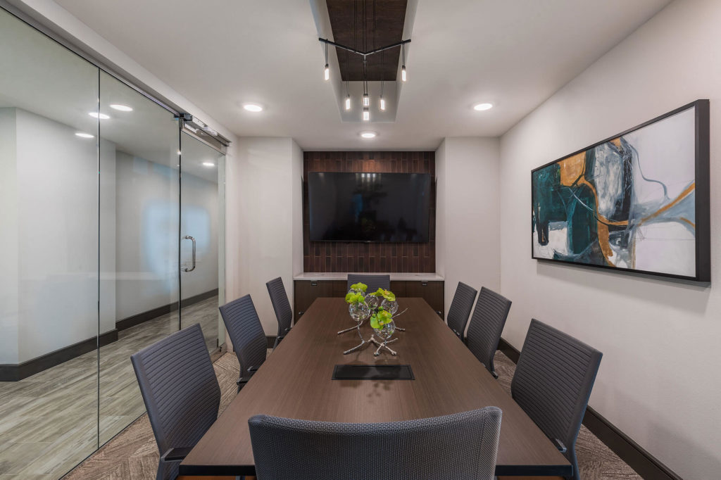 Conference area with long table, 8 chairs, flat-screen tv, decorative lighting and large enclosed glass doors