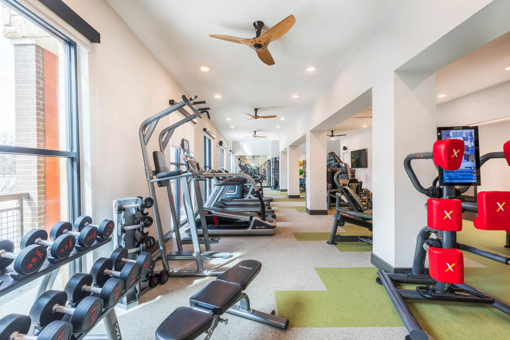 Fitness center with free weights, bench, weight machine, cardio machines, and ceiling fans
