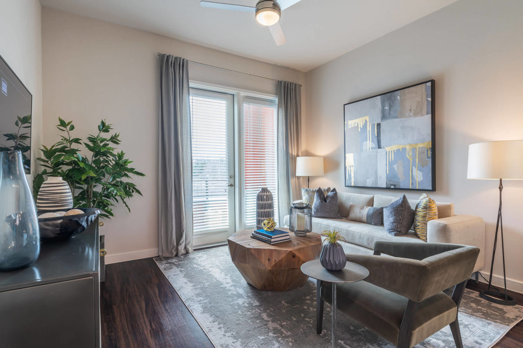 Living area with wood-style floors, ceiling fan, door to balcony, large TV, and modern furniture