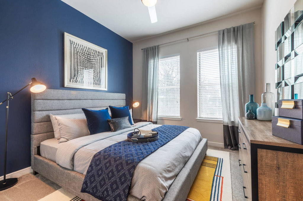 Bedroom with king-sized bed, 2 windows, ceiling fan, blue accent wall, and large dresser