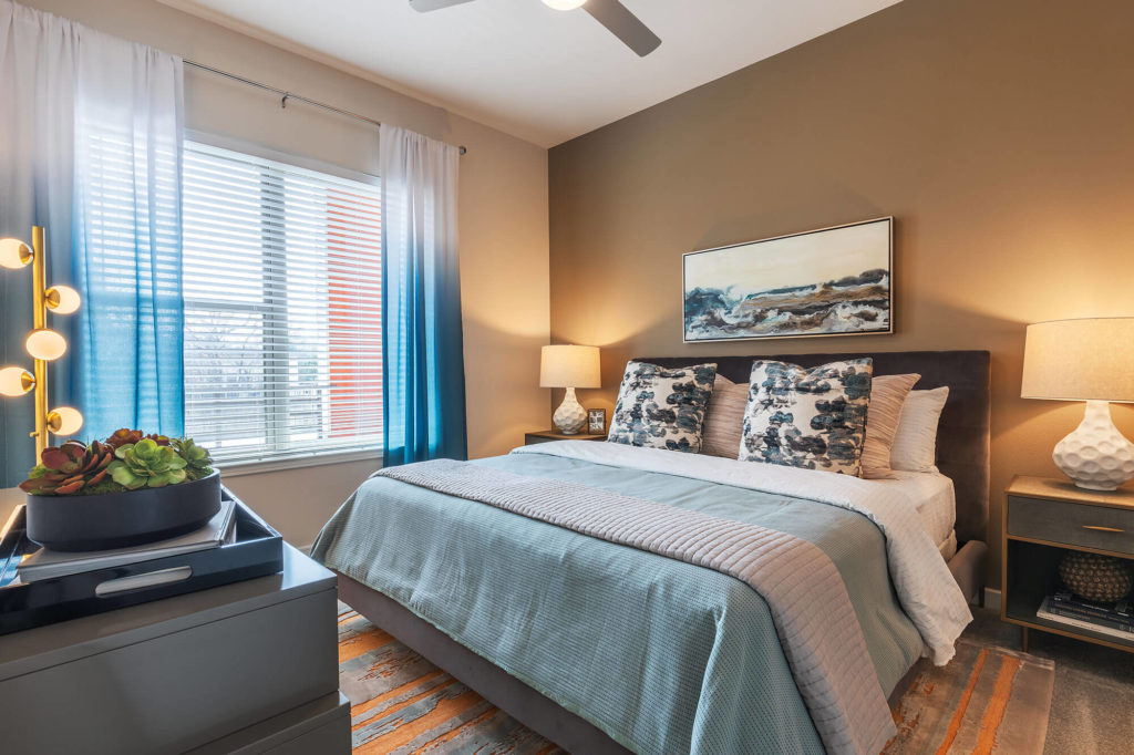 Bedroom with plush carpeting, ceiling fan, king-size bed, large window, night stands, dresser, and accent wall