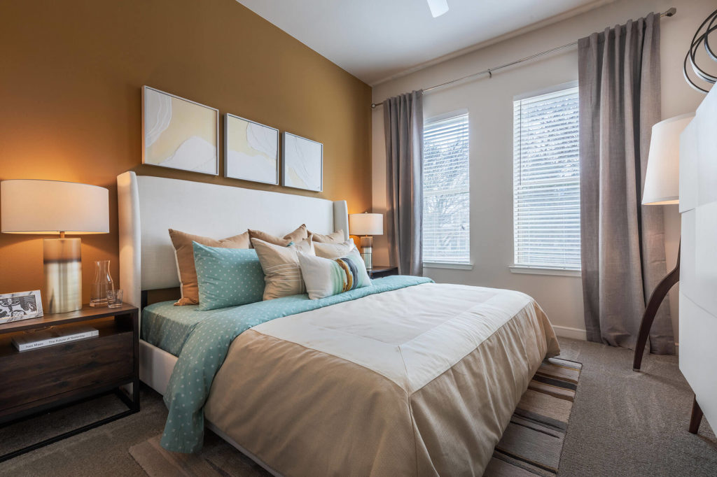 Bedroom with king size bed, plush carpeting, 2 windows, nightstands, and orange accent wall