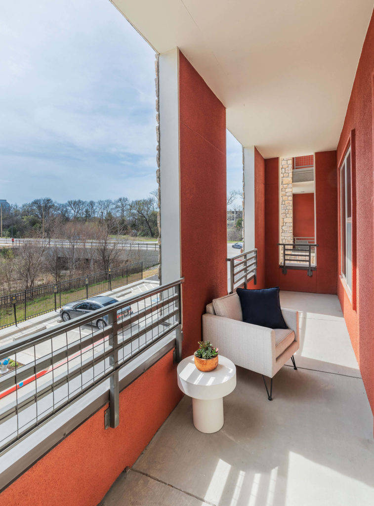 Apartment balcony with table and chair, safety rails, decorative color stucco, and expansive views